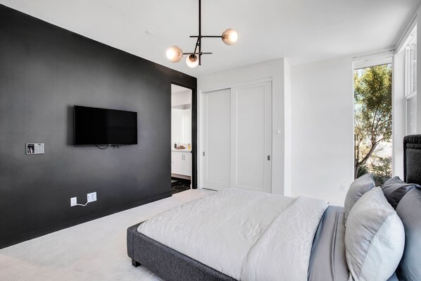 A modern bedroom with a large bed, a flat-screen TV mounted on the wall, and a ceiling light fixture. - Modern mountain-view gem with private pool, jacuzzi, & resort amenities (Palm Springs)