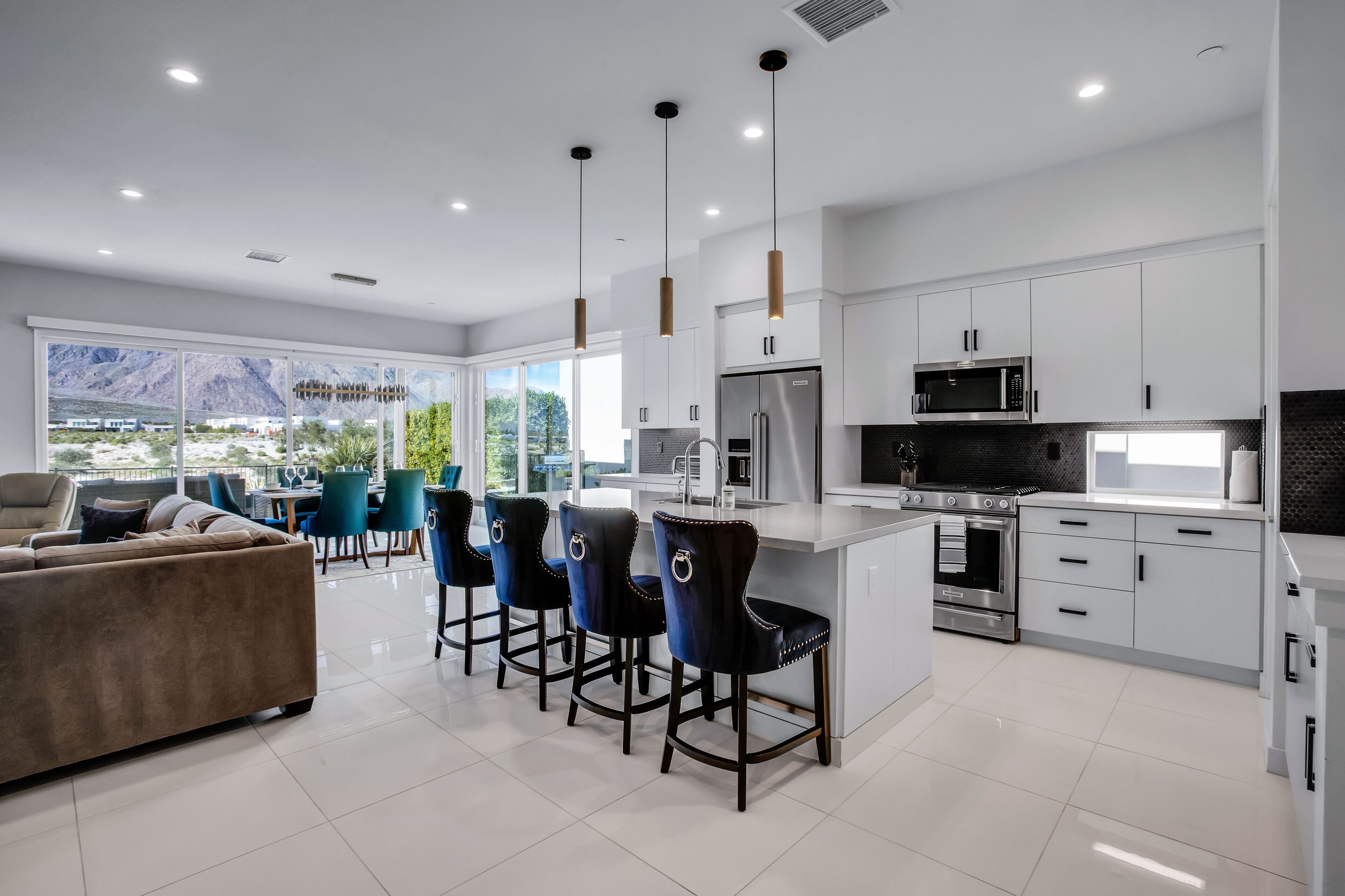 Cocina moderna con armarios blancos, electrodomésticos de acero inoxidable y una barra con taburetes negros.