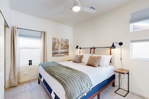 Une chambre à coucher comprenant un lit, une table de chevet, un ventilateur de plafond, une fenêtre avec des rideaux et une lampe fixée au mur.