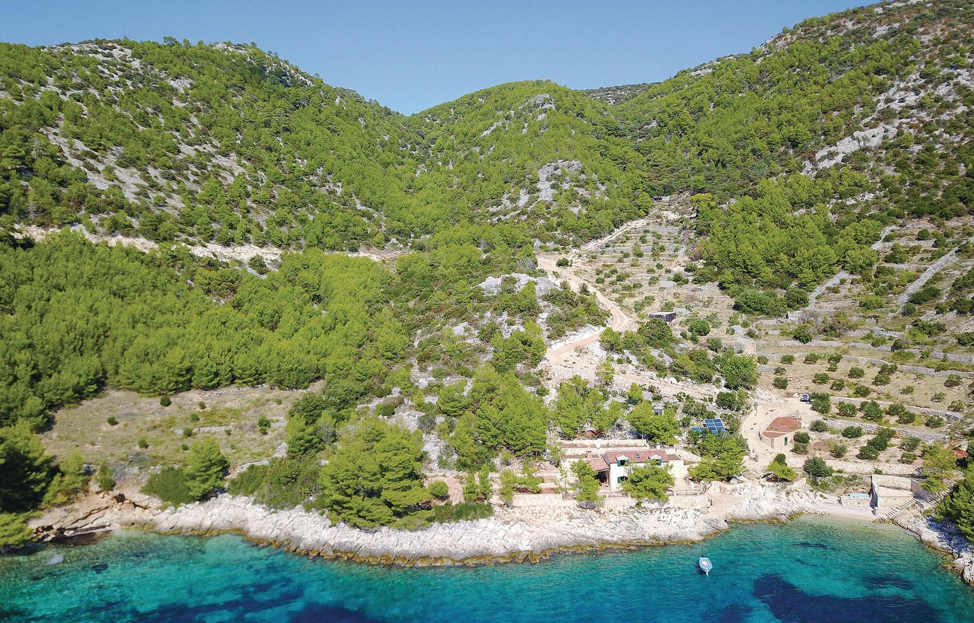A coastal area with a rocky shoreline, clear turquoise waters, and a small building with a red roof near the beach.