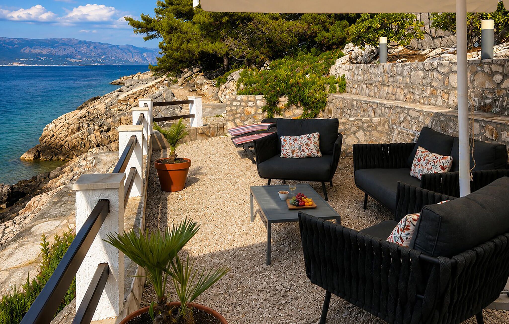 An outdoor seating area with a stone wall, a view of the sea, and a potted plant.