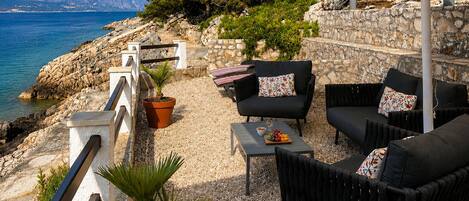 An outdoor seating area with a stone wall, a view of the sea, and a potted plant.