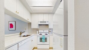 Een moderne keuken met witte kastjes, een roestvrijstalen spoelbak en een magnetron boven het fornuis.