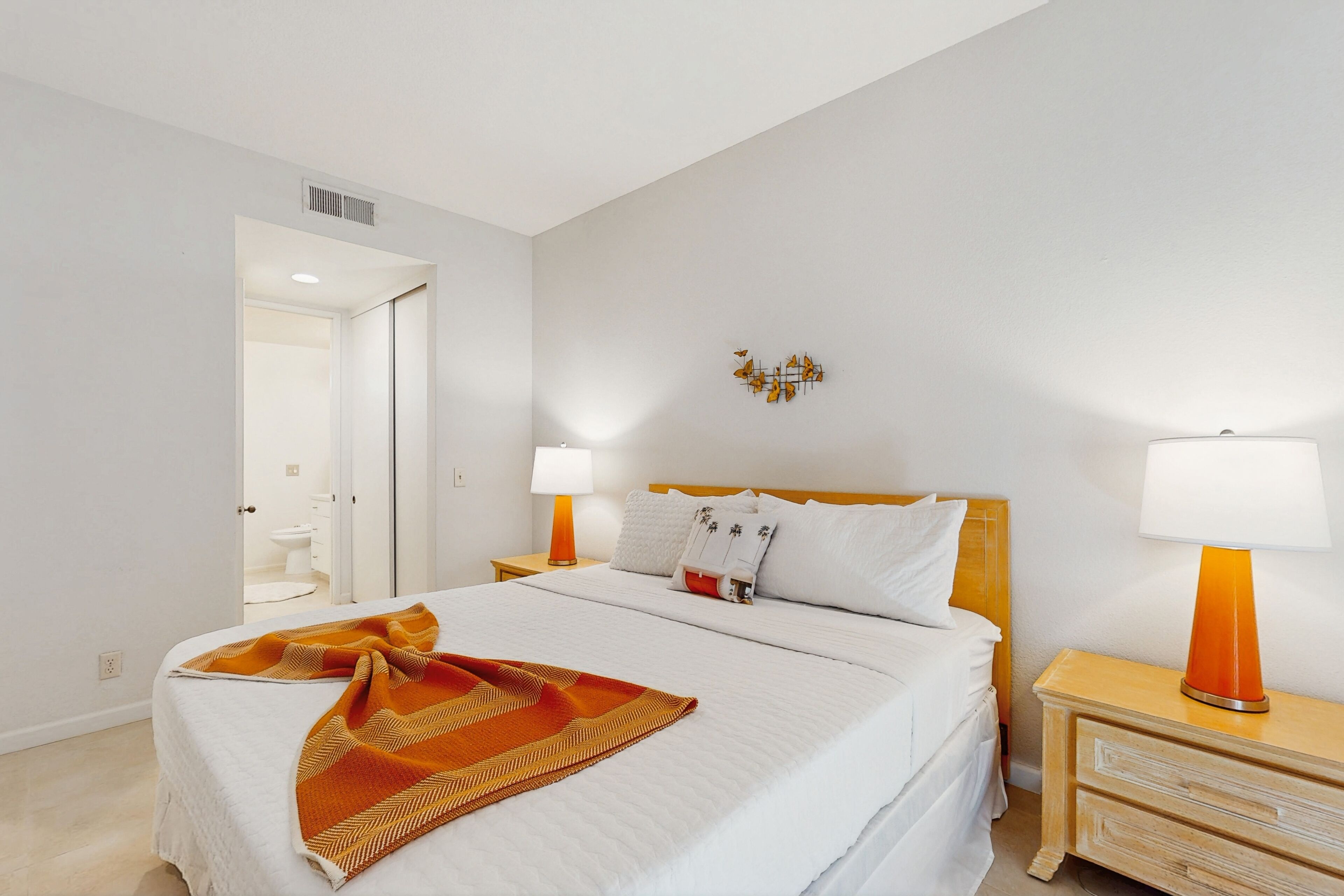 A hotel room with a bed, two bedside tables, a nightstand, a wall-mounted light fixture, and a door leading to a bathroom.