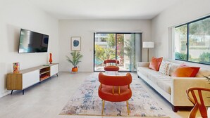 Een moderne woonkamer met een bank, een rode stoel, een televisie en een groot raam.