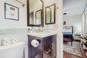 A modern bathroom with a toilet, sink, and mirrors. There is a framed picture on the wall and a bed in the adjacent room. - Your Perfect Family Getaway in Tempe - Comfort, Fun, Outdoor Pool, and Sun Await (Tempe)
