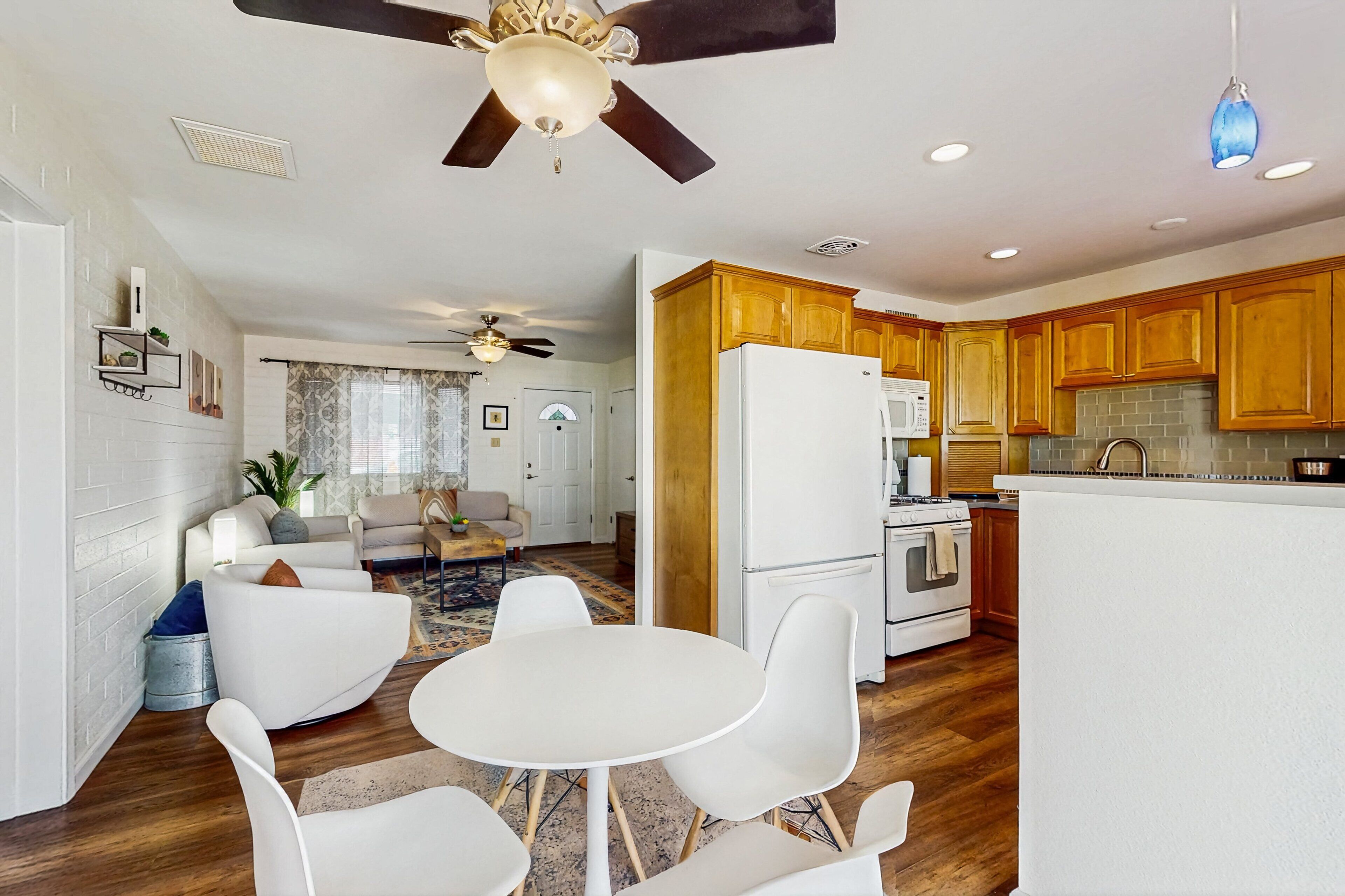 A modern kitchen with wooden cabinets, a white refrigerator, and a dining area with white chairs and a round table.
