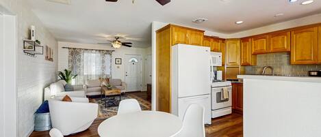 A modern kitchen with wooden cabinets, a white refrigerator, and a dining area with white chairs and a round table.