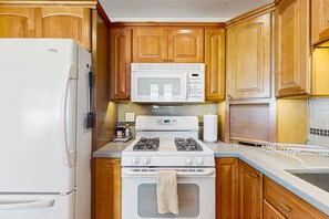 Une cuisine avec des meubles de rangement en bois, un réfrigérateur blanc, un four à micro-ondes, une cuisinière et un évier.