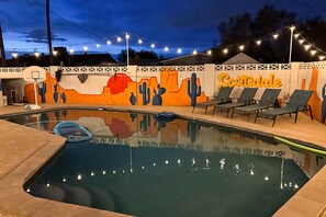 Une piscine agrémentée d’une fresque murale, de chaises longues et de guirlandes lumineuses.