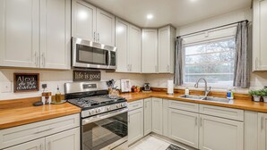 Een moderne keuken met witte kasten, roestvrijstalen apparatuur en een raam met jaloezieën.