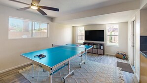 Una habitación con mesa de ping pong, ventilador de techo, ventanas amplias y televisor.