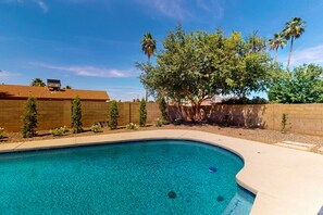 A clear blue swimming pool with a curved edge, surrounded by a brick wall and small trees. - Modern home with private pool, covered patio, & ping-pong table - dogs ok (Scottsdale)