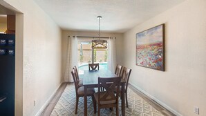 Un comedor con una mesa y sillas, una lámpara en el techo, un cuadro en la pared y vistas al exterior.