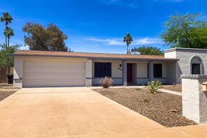 A single-story house with a garage, a small front yard with gravel and a few plants, and a clear blue sky. - Modern home with private pool, covered patio, & ping-pong table - dogs ok (Scottsdale)