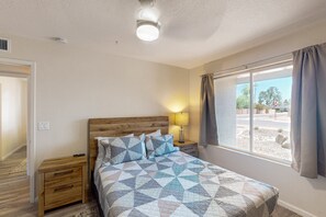 A bedroom with a wooden headboard, a bed with a geometric patterned bedspread, a nightstand with a lamp, and a window with curtains. - Modern home with private pool, covered patio, & ping-pong table - dogs ok (Scottsdale)