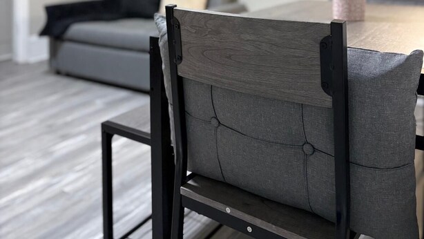 Ein Essbereich mit Tisch und Stühlen, einem grauen Sofa und einer kleinen Pflanze auf dem Tisch.