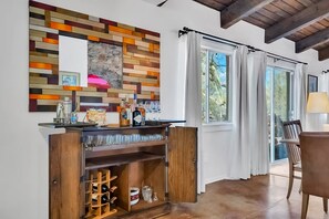 A modern living room with a wooden bar area, large windows with curtains, and a dining table with chairs. - Ranch Style Living in Catalina Foothills with private hot tub (Tucson)