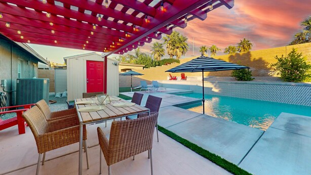 Een terras buiten met een zwembad, rieten meubels en een rode pergola.
