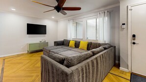 Een moderne woonkamer met een modulaire bank, plafondventilator, televisie en een groene kast.