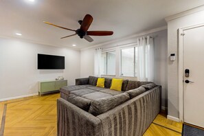 Ein modernes Wohnzimmer mit einem Ecksofa, Deckenventilator, Fernseher und einem grünen Schrank.