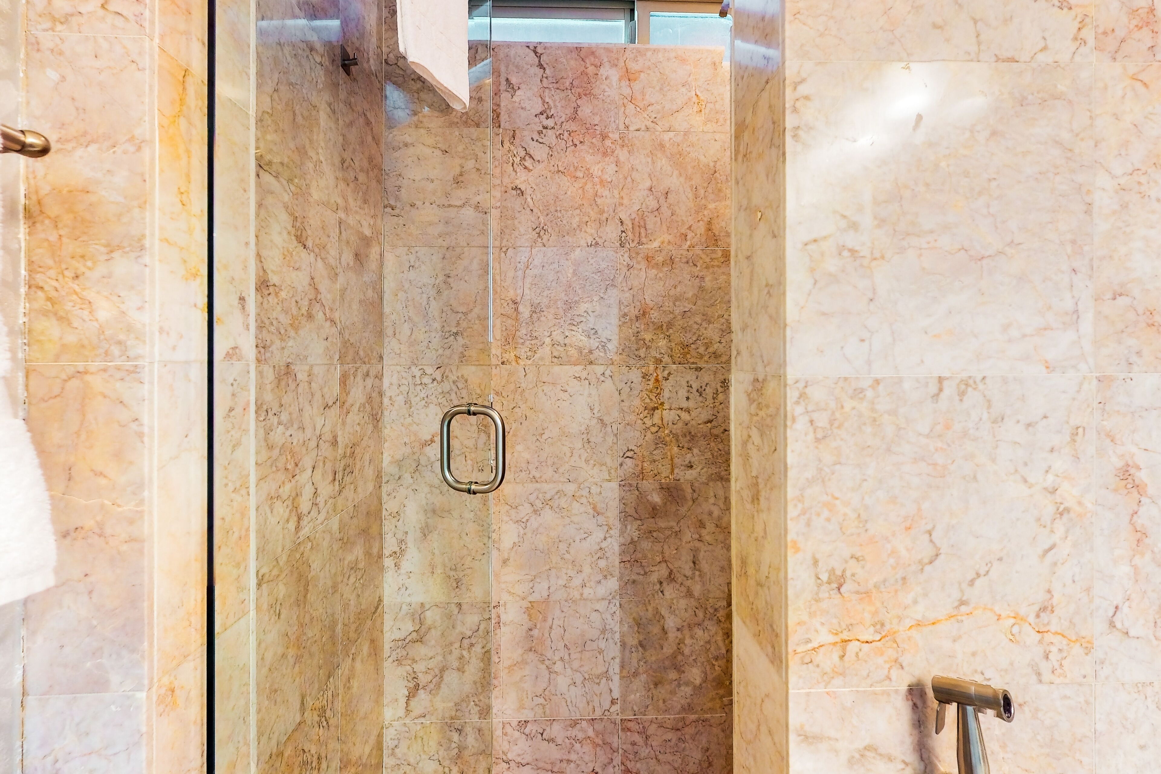 Un bany amb rajoles de marbre, una cabina de dutxa de vidre i un suport per a tovalloles.