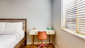Een slaapkamer met een bed, een bureau, een stoel en een raam met zonwering.