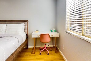 Ein Schlafzimmer mit einem Bett, einem Schreibtisch, einem Stuhl und einem Fenster mit Jalousien.