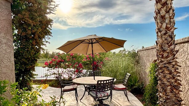 Een terras met een ronde tafel, stoelen, een parasol en een palmbom.