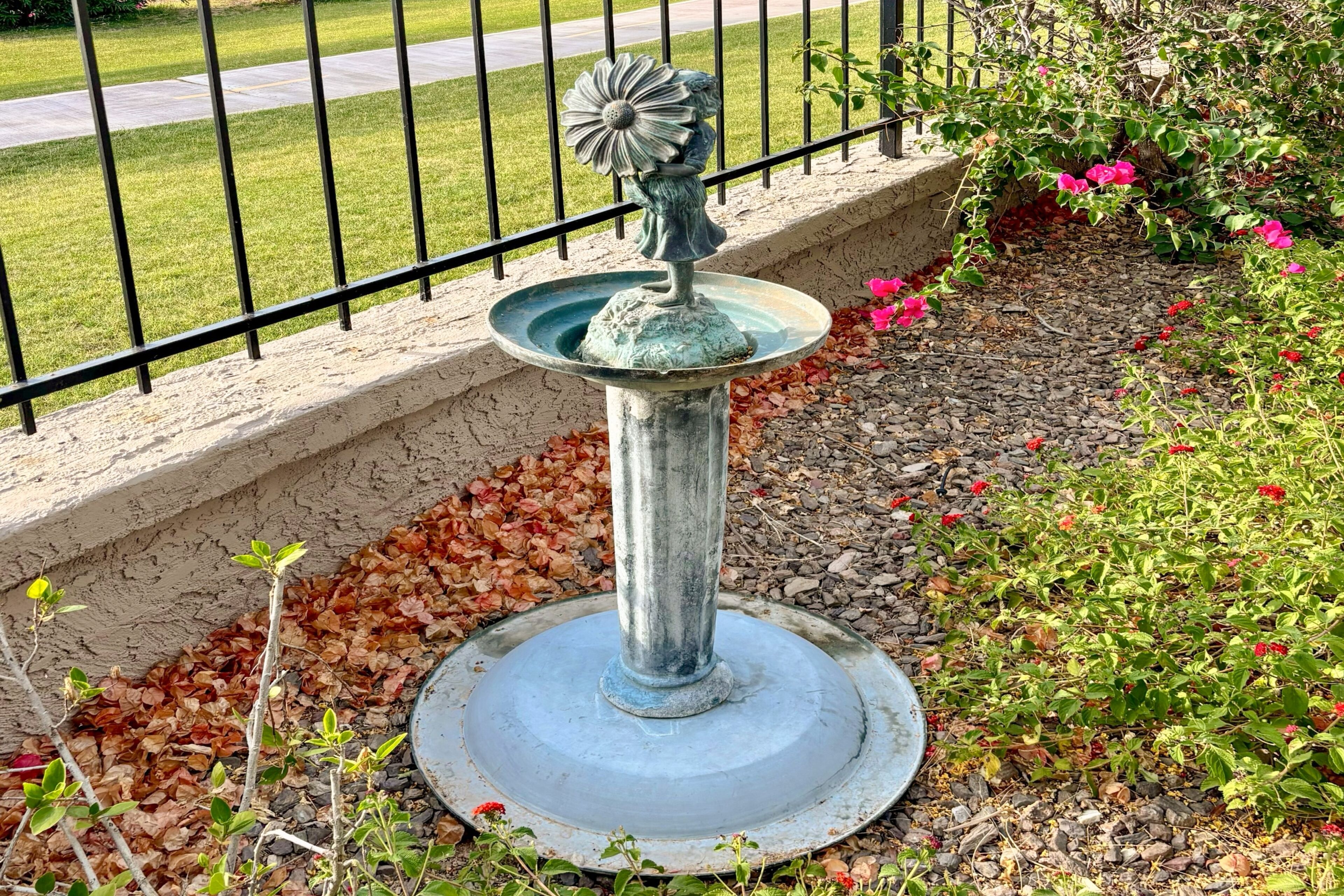 A garden with a metal fountain, surrounded by a stone border and various plants.