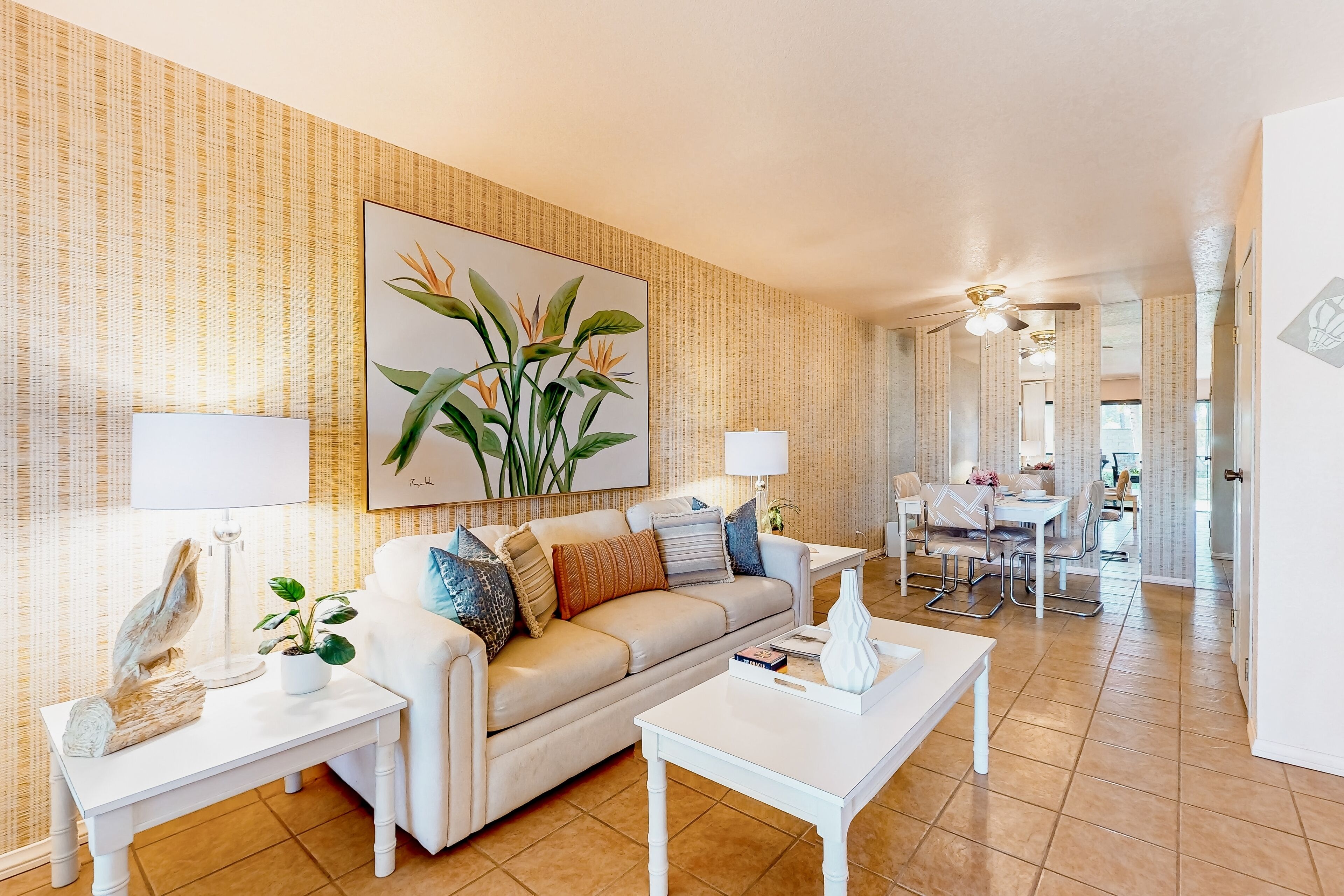 A living room with a beige sofa, white coffee table, and a dining area with a white table and chairs.