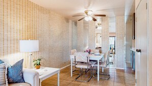 Uma sala de estar moderna com área de jantar, apresentando um ventilador de teto, uma mesa branca e um sofá com almofadas estampadas.