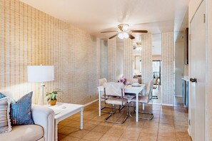 A modern living room with a dining area, featuring a ceiling fan, a white table, and a sofa with patterned cushions. - Snowbird-friendly retreat with pool, hot tub, tennis, putting green, & patio (Palm Springs)
