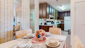 Uma área de refeições com uma mesa posta para quatro pessoas, rodeada por cadeiras estampadas. Um centro de mesa decorativo está sobre a mesa.