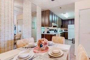 A dining area with a table set for four, surrounded by patterned chairs. A decorative centerpiece is on the table. - Snowbird-friendly retreat with pool, hot tub, tennis, putting green, & patio (Palm Springs)