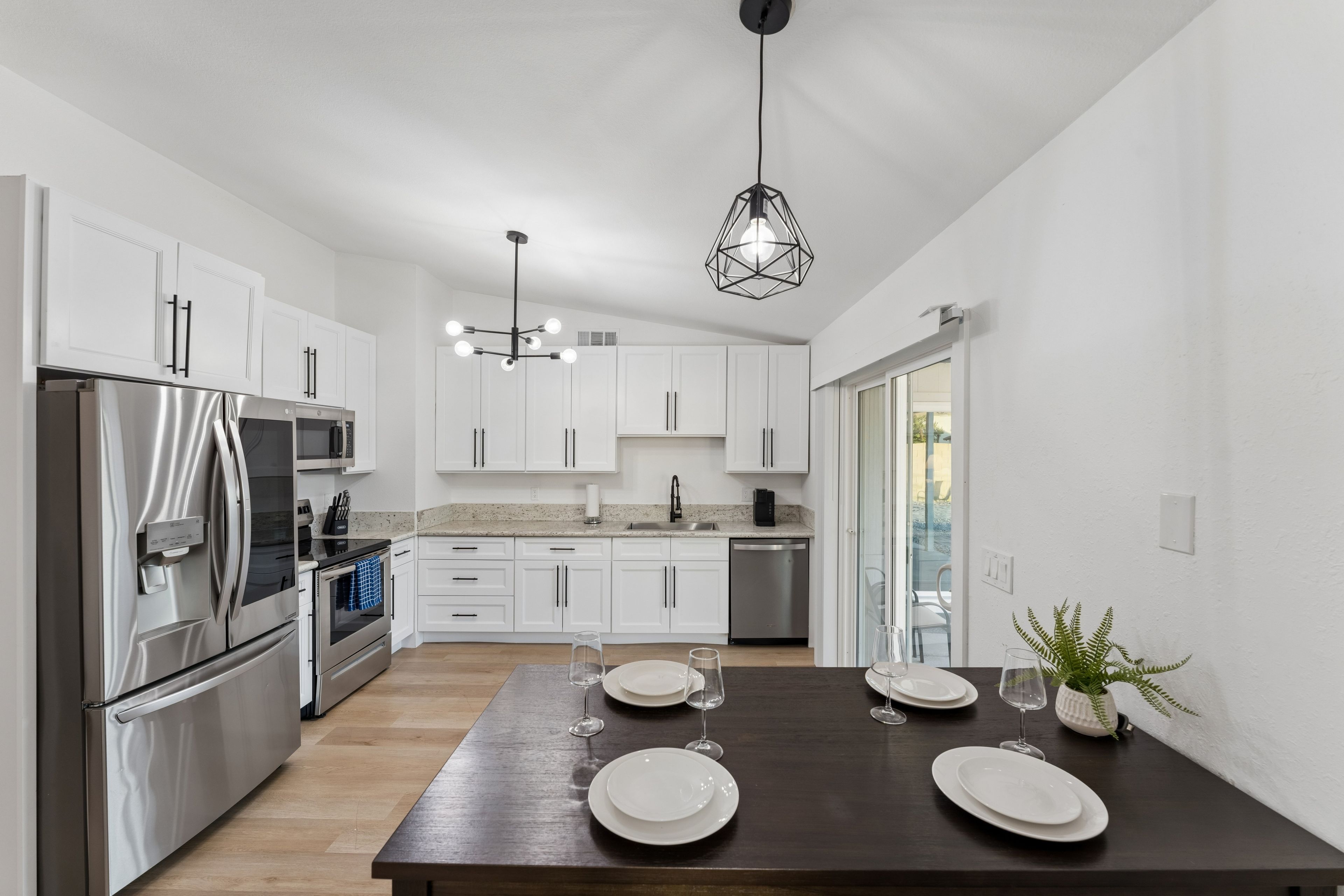 A modern kitchen with white cabinets, stainless steel appliances, and a dark wooden dining table set for two.