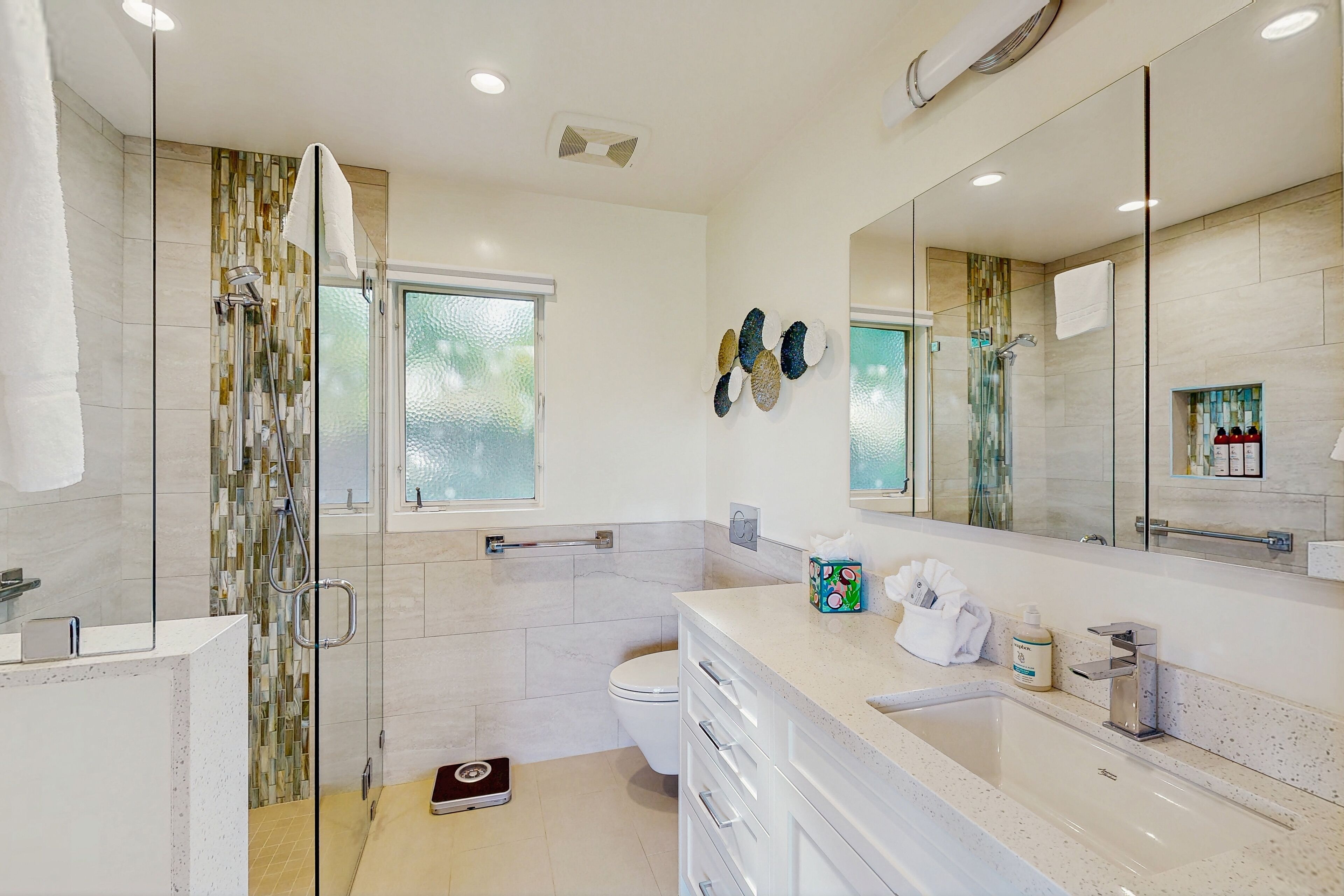 Un baño moderno con ducha envuelta en vidrio, inodoro y tocador con lavamanos y espejo.
