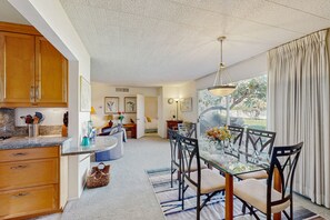 A modern kitchen with wooden cabinets, a granite countertop, and a dining area with a glass table and chairs. - Sunny Palm Springs Retreat with Shared Pool, Hot Tub & Prime Location! (Palm Springs)