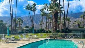 A swimming pool with lounge chairs and umbrellas, surrounded by palm trees and mountains in the background. - Sunny Palm Springs Retreat with Shared Pool, Hot Tub & Prime Location! (Palm Springs)