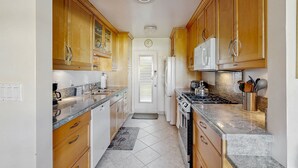 A narrow kitchen with wooden cabinets, a stove, a microwave, and a refrigerator. - Sunny Palm Springs Retreat with Shared Pool, Hot Tub & Prime Location! (Palm Springs)