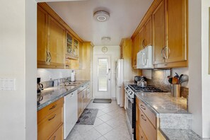A narrow kitchen with wooden cabinets, a stove, a microwave, and a refrigerator. - Sunny Palm Springs Retreat with Shared Pool, Hot Tub & Prime Location! (Palm Springs)