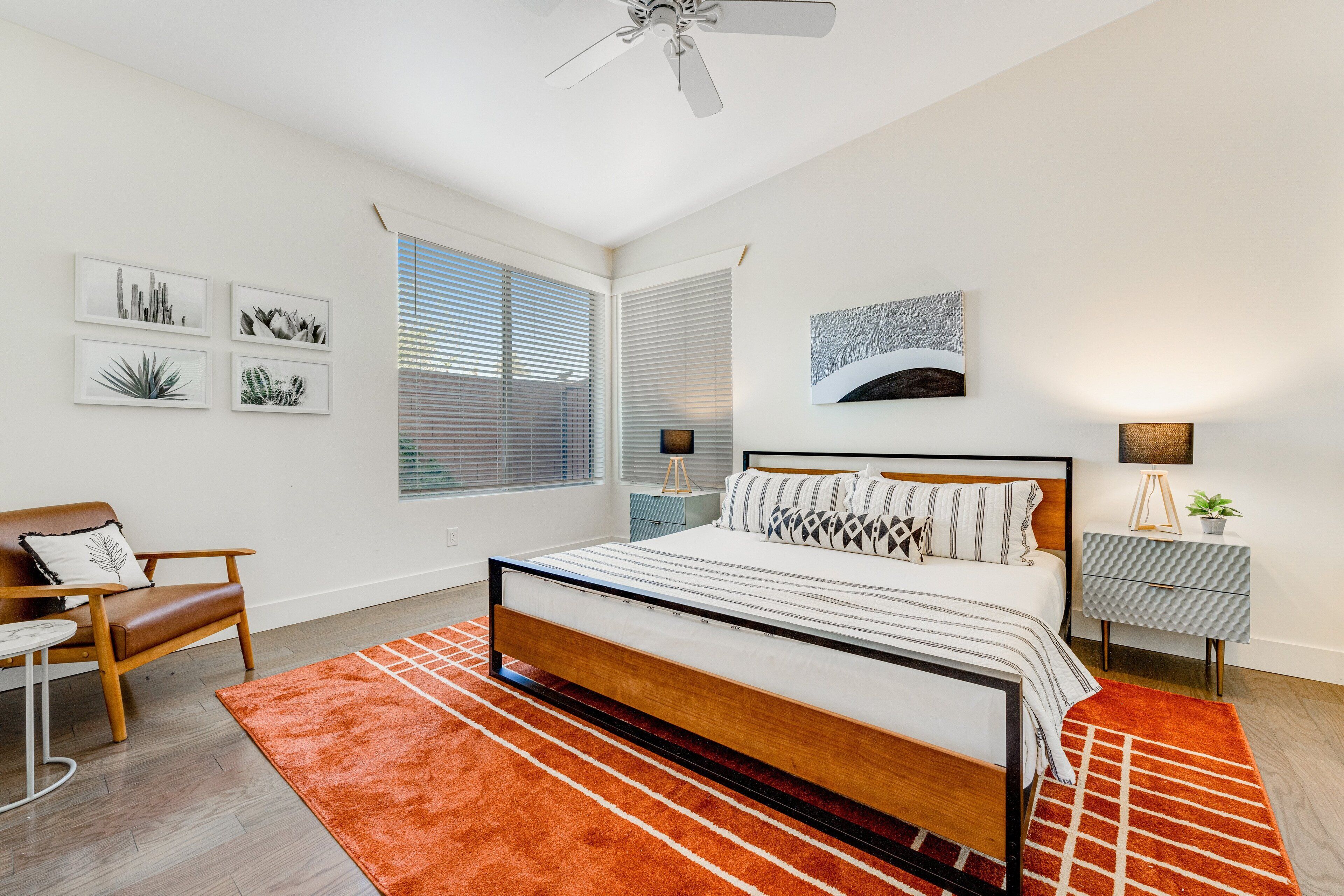 A modern bedroom with a wooden bed, a red rug, a chair, a nightstand, and wall art.