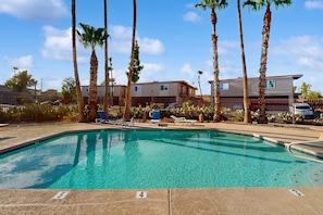 A swimming pool with lounge chairs and palm trees, surrounded by a fence and buildings in the background. - Modern townhome with pool, AC, W/D, grill, and private patio (Fountain Hills)