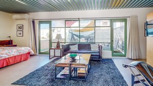 Una habitación moderna con cama, sofá, una mesa de centro de vidrio y vistas a través de amplios ventanales.