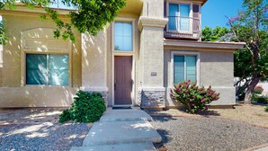 A two-story building with a front door, a small balcony, and a gravel driveway. - Airy home with private heated pool, firepit, grill, enclosed backyard, cornhole (Goodyear)