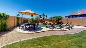 A backyard with a pool, patio furniture, and a brick wall. - Airy home with private heated pool, firepit, grill, enclosed backyard, cornhole (Goodyear)