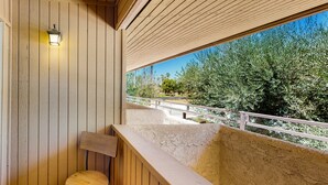Un balcon en bois avec une chaise en bois, un luminaire et une vue sur des arbres et un sentier.