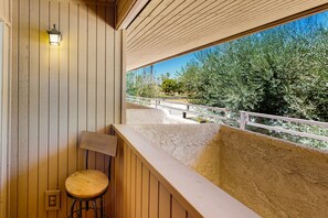 Ein Holzbalkon mit einem Holzstuhl, einer Lampe und Blick auf Bäume und einen Weg.
