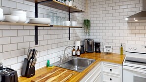 Une cuisine dotée d’un plan de travail en bois, d’un évier en acier inoxydable, de meubles blancs et d’une machine à café.