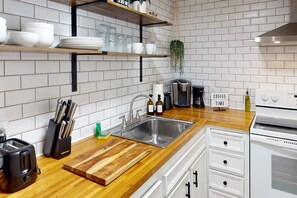Eine Küche mit einer Holzarbeitsplatte, einem Edelstahlspülbecken, weißen Schränken und einer Kaffeemaschine.
